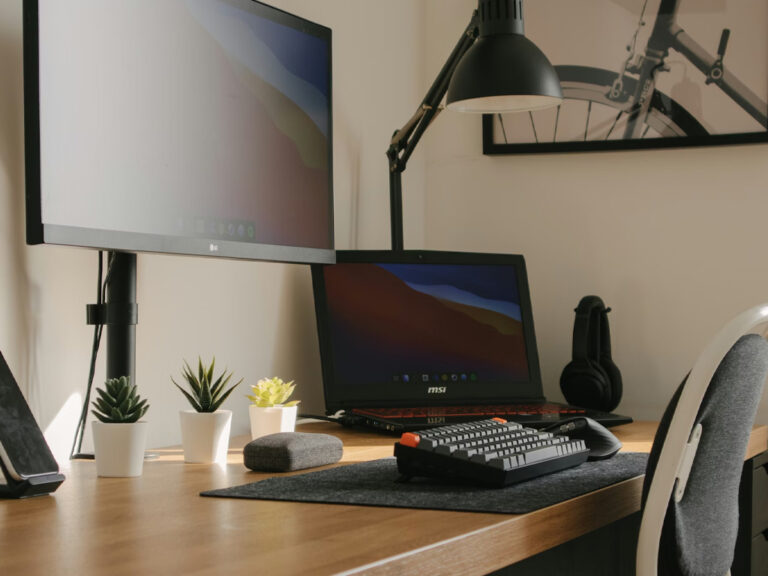 A small home office, with a computer, second screen and lamp, along with other desk decor